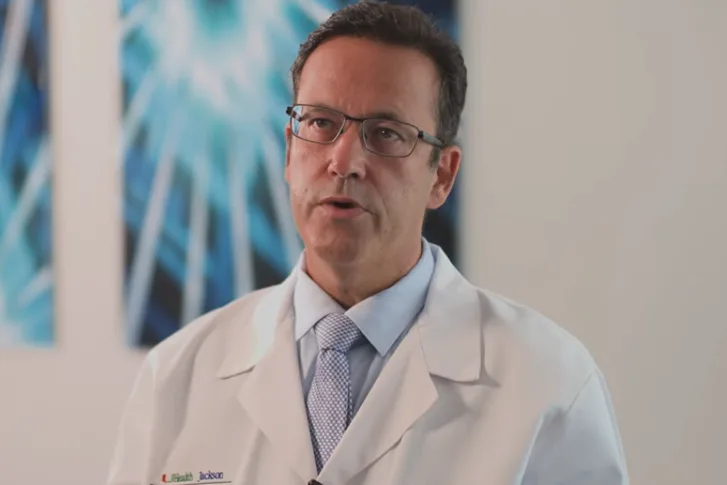 A medical professional speaking, he has on a white coat and glasses