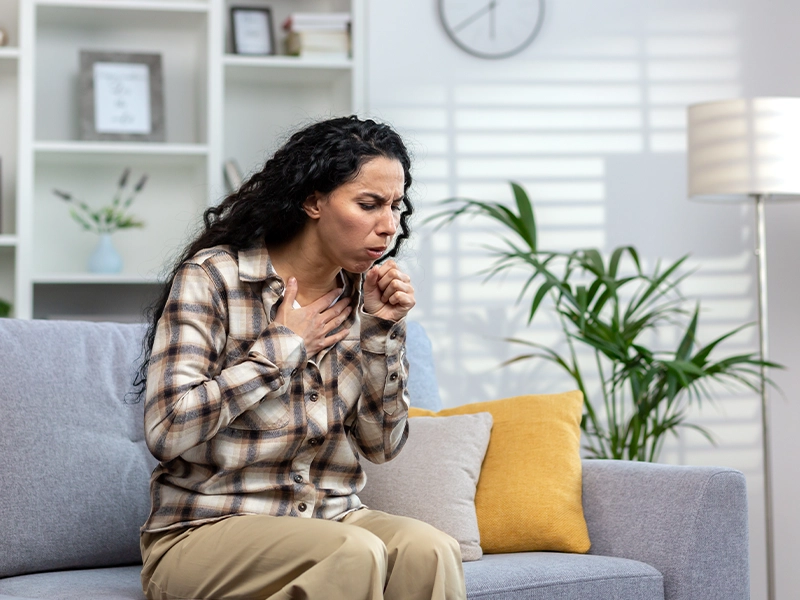 woman sitting on a sofa while coughing