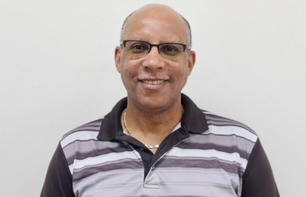A closeup of a man, he smiles at the camera, he has on glasses and a collared shirt