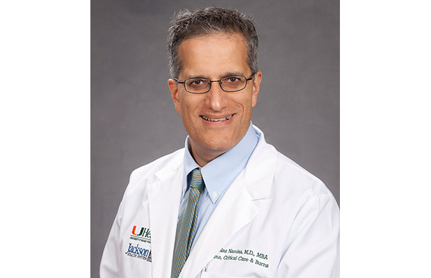A headshot of a physician, he is smiling at the camera, he has on black trimmed glasses and white coat