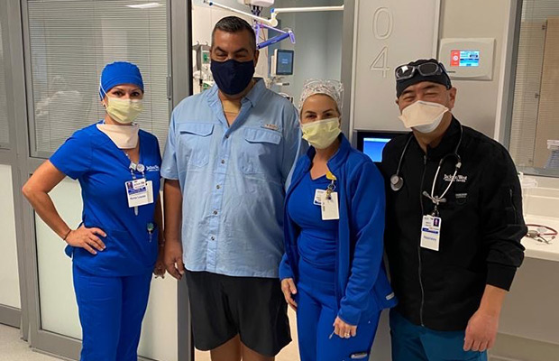 A man and three healthcare professionals standing inside a medical building, they all wear face masks and look towards the camera