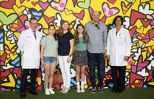 A group of people and medical professionals standing in front of a colorful wall, they smile at the camera