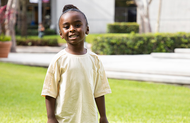 A young child smiling at the camera, he is standing outdoors