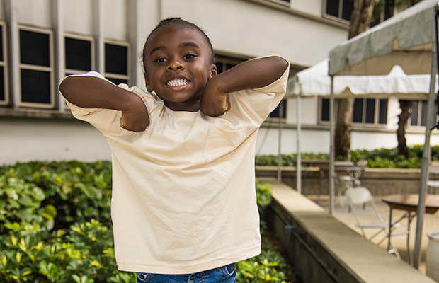 A young boy smiling at the camera, he is standing outdoors