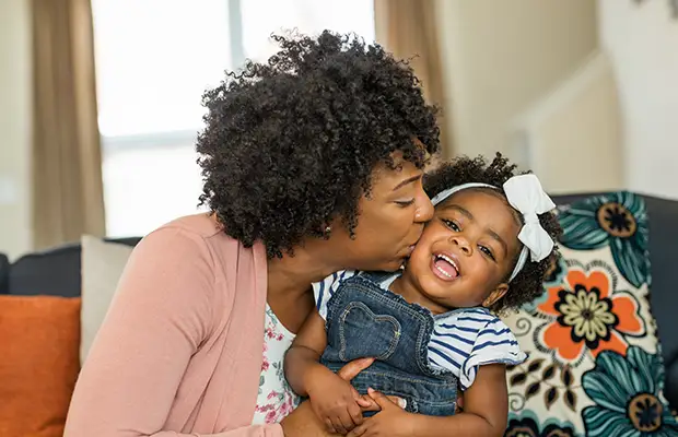 Mom hugging and kissing her daughter on her cheek
