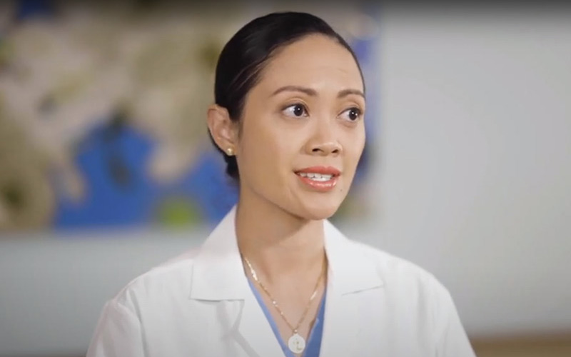 Closeup of a physician, she wears a white coat, has her hair up and looks towards her left
