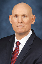 Headshot of David Ewing, he is looking at the camera, he has on a dark jacket, white shirt, and red tie