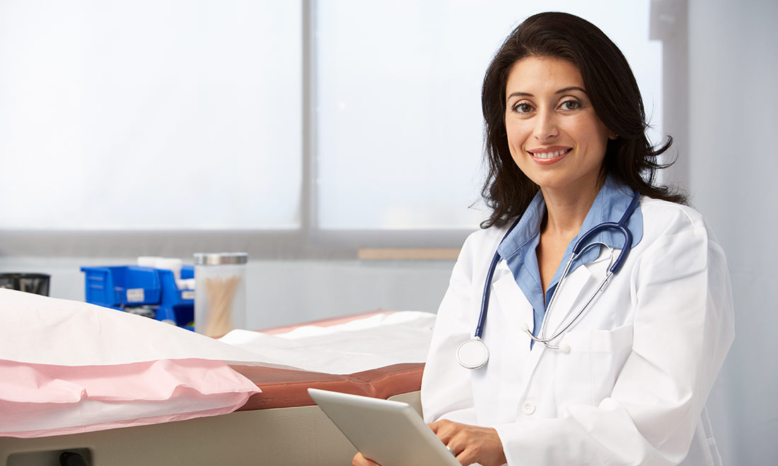 Doctor holding a tablet in a medical room, she is holding a tablet and smiling at the camera