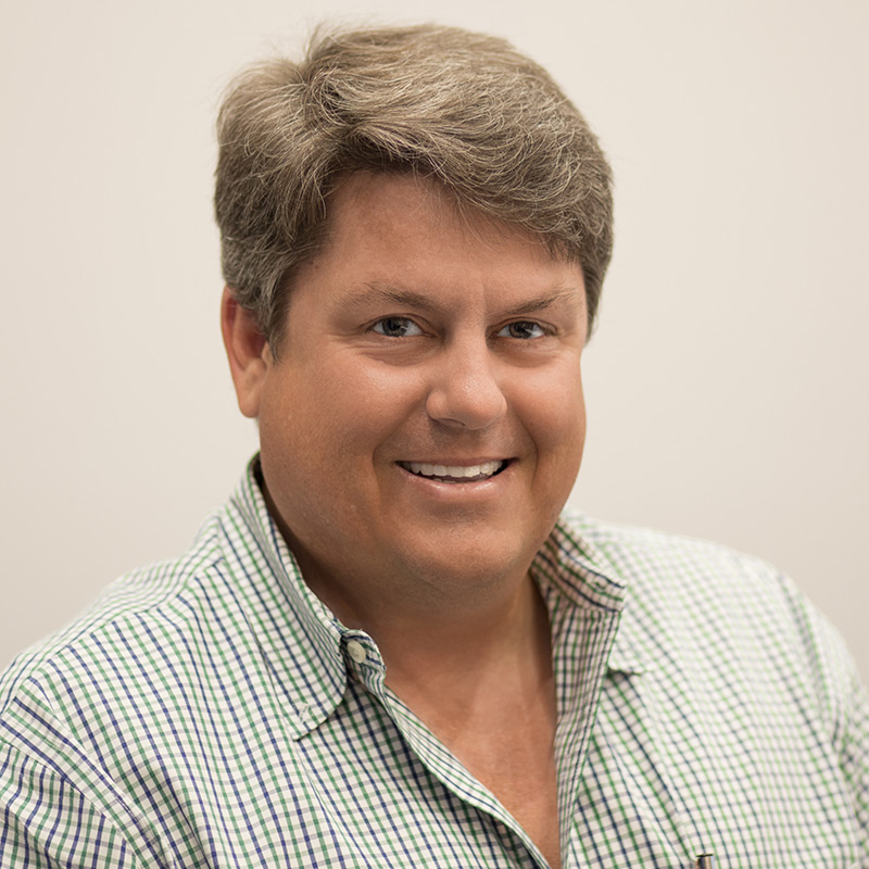 Closeup of a man smiling at the camera, he is wearing a green collared checkered shirt