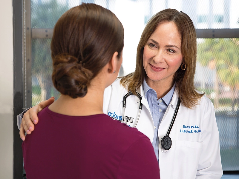 A female physician smiling at her female patient as she puts her right hand on her patients shoulder