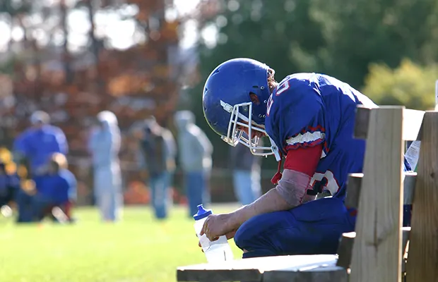 A football player sitting on a bench, looking down