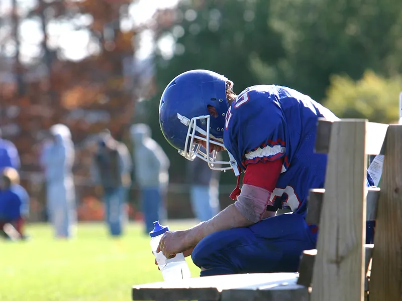 A football player sitting on a bench, looking down