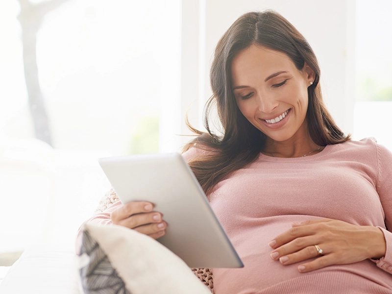 Pregnant Spanish woman touching her stomach as she looks at her tablet device