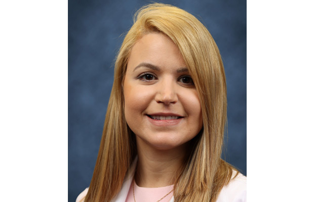 A headshot of a physician, she has long red hair and smiles at the camera