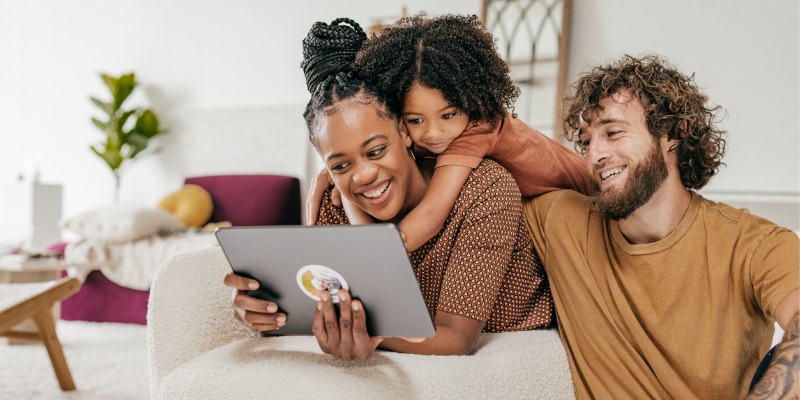A family of three, a woman, man, and young girl are sitting together and looking at a computer screen
