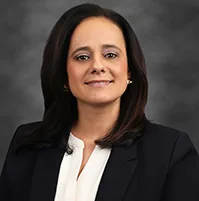 Woman smiling at the camera, she has on a dark coat and white blouse
