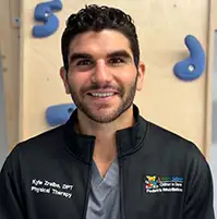 A medical professional smiling at the camera, he has on gray scrubs and a black jacket