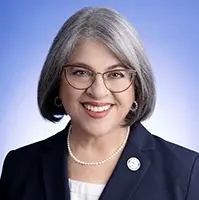 A closeup of a women, she smiles at the camera, she has on a white top and blue jacket