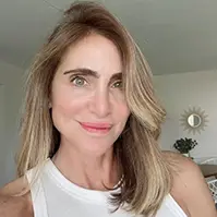 A closeup of a women, she smiles at the camera, she has on a white top