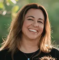 A closeup of a woman, she smiles at the camera, she has long brown hair and a dark shirt