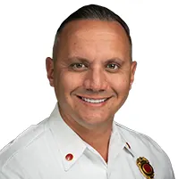 A man smiling at the camera, he has short hair and a white professional attire