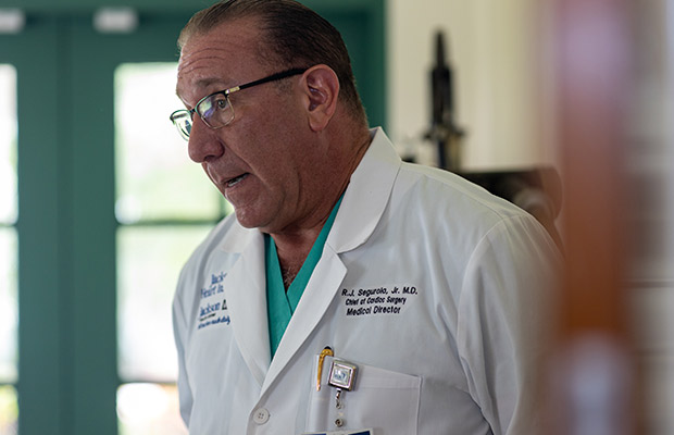 A closeup of a physician, he is wearing glasses and a white coat