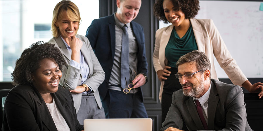 Five coworkers standing and sitting next to each other as they look at a laptop screen