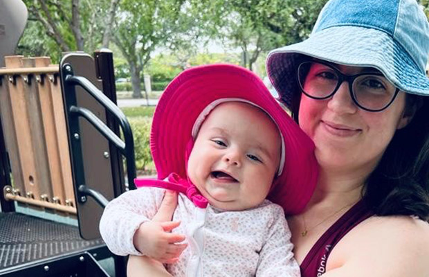 A woman holding a smiling baby, they are outdoors