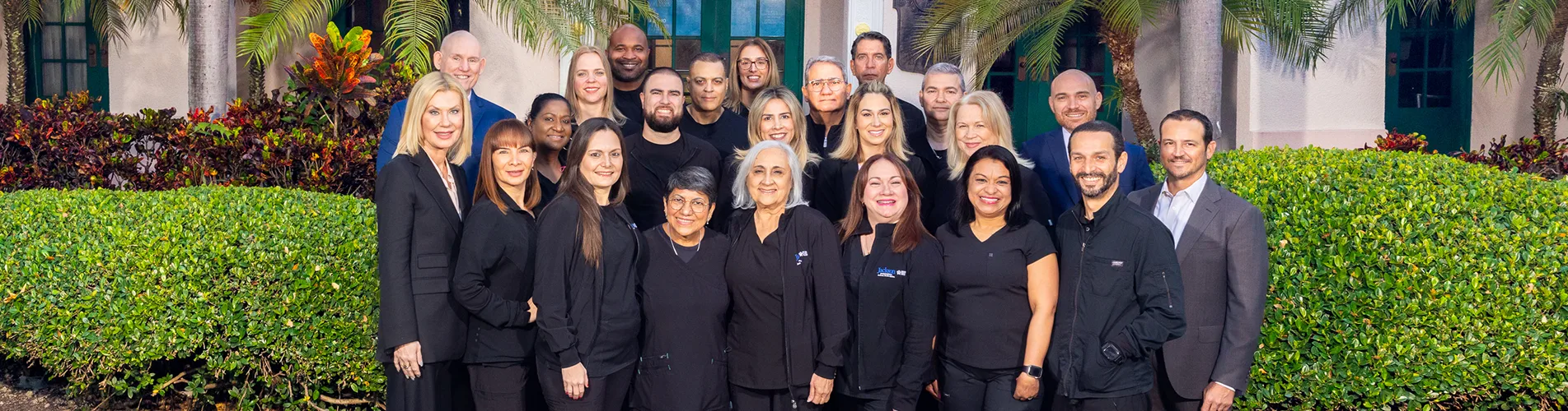 A large group of medical professionals, they stand in front of a building, they smile at the camera