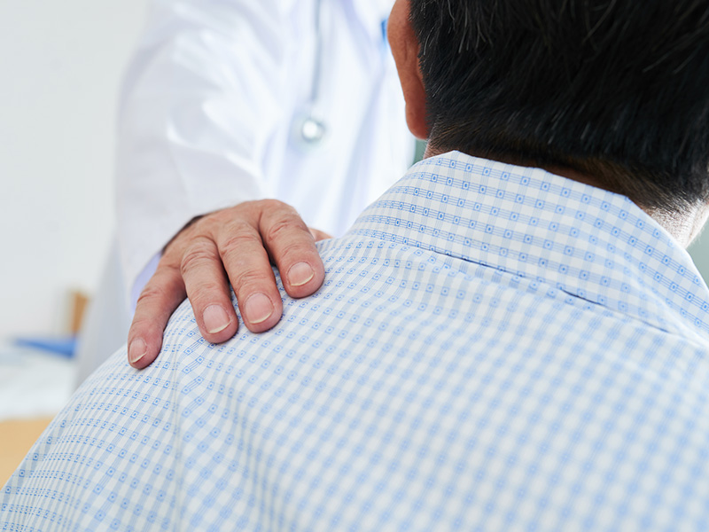 Closeup of a doctors hand on a male patients left shoulder