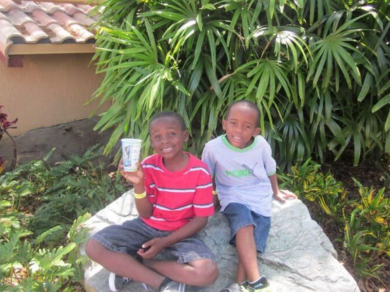 Two children sitting on a rock, smiling at the camera
