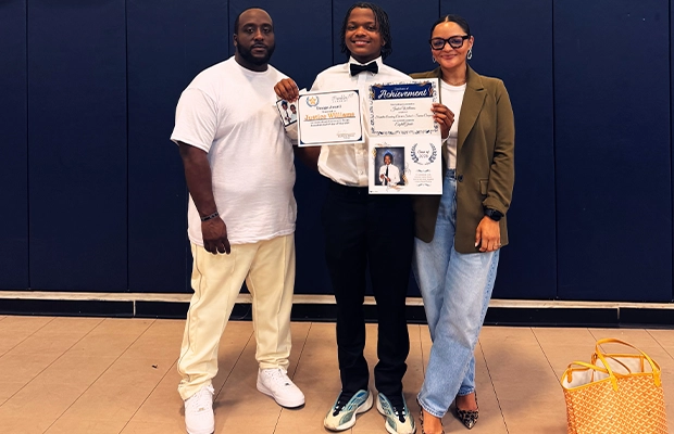 Young man posing with two people on his graduation day.