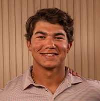 Close-up of a smiling man wearing a pink T-shirt.