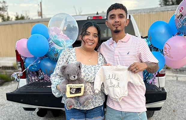 A couple showing baby clothes and accessories to the camera