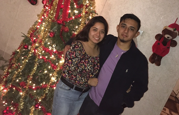 Photograph of a couple smiling at the camera next to a Christmas tree