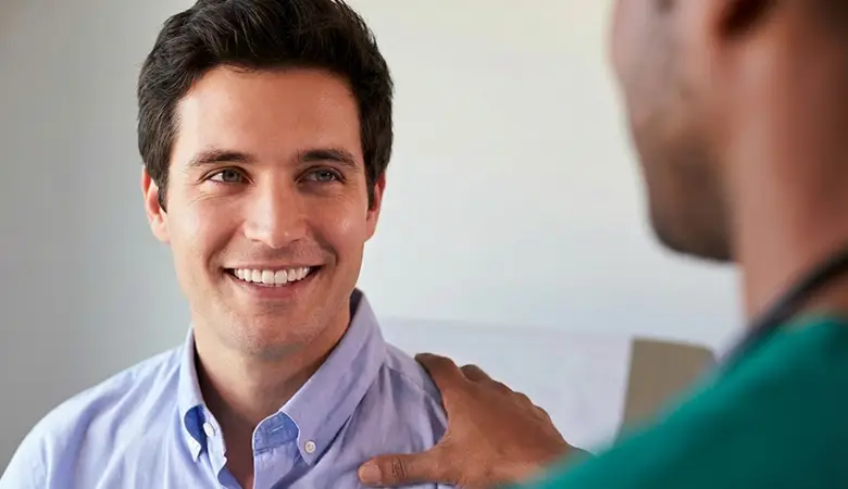 A middle aged man smiling as he looks at a medical professional who has their right hand on their left shoulder