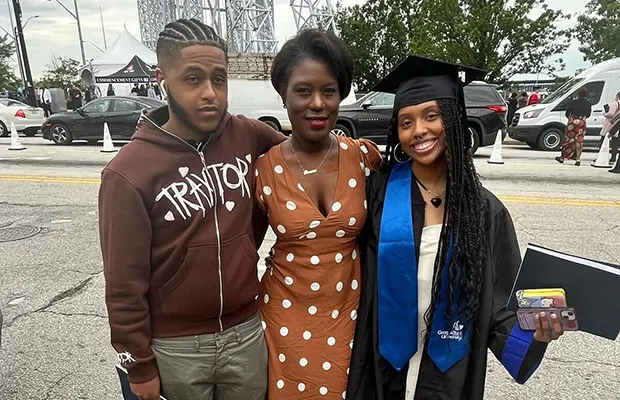 A group of three people, one of them is wearing graduate attire