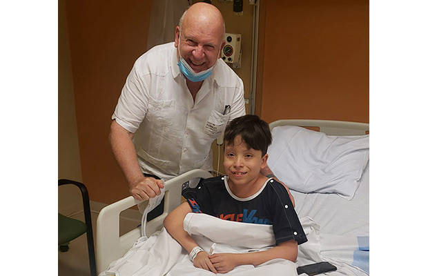 A young boy in a hospital bed, he is sitting up and smiling, there is an older man next to him smiling