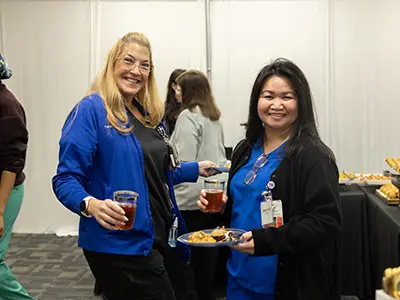 Two medical professionals smiling at the camera, they are holding drinks and food