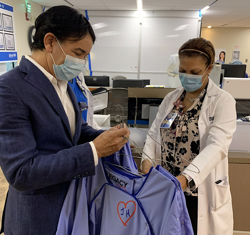 A physician looking at hospital gowns, there is a man next to her who is holding the gowns and looking down at them