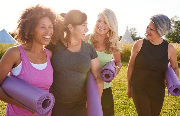 Four adult women walking in the park with yoga implements