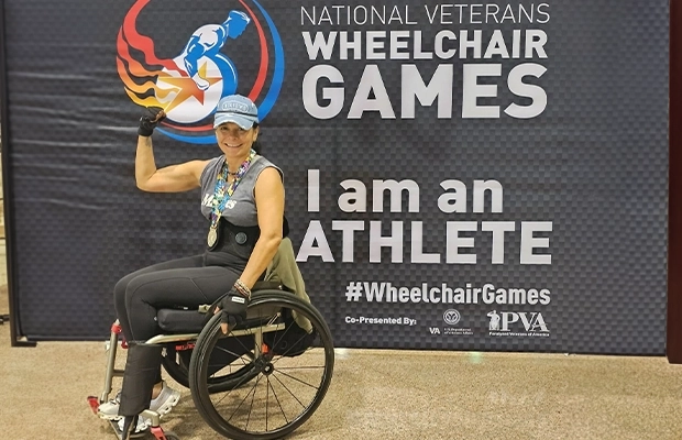 mujer posando en silla de ruedas junto a letrero que dice National veteranos wheelchair games