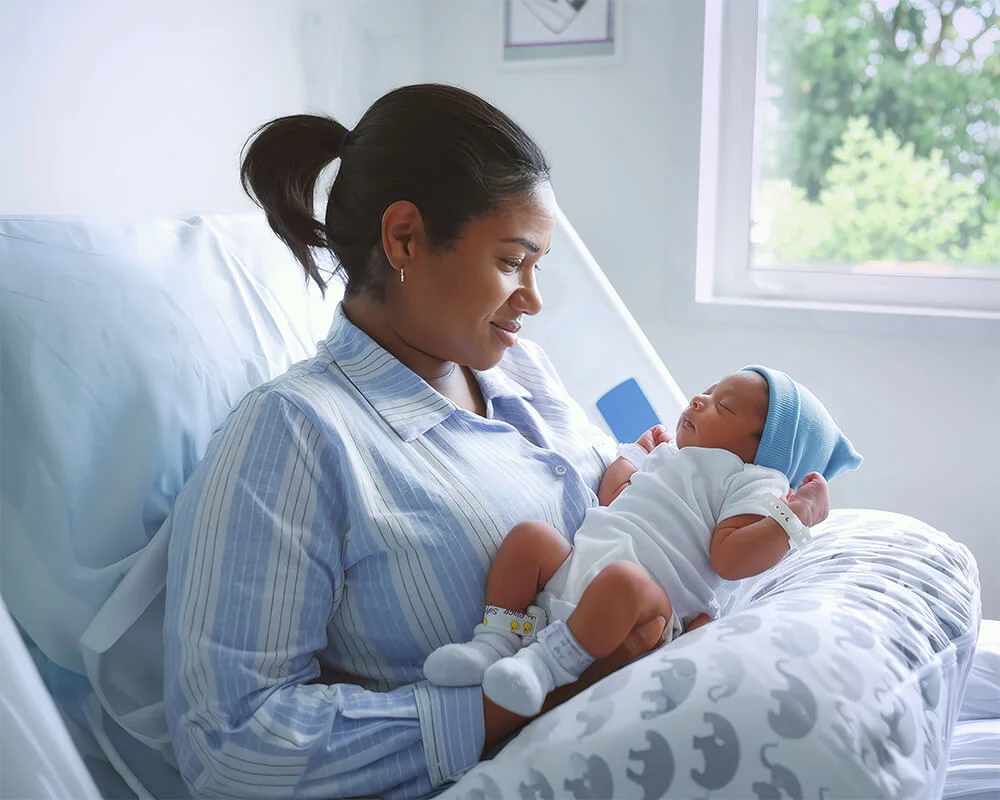 A woman sitting on the hospital bed while holding up her newborn baby.
