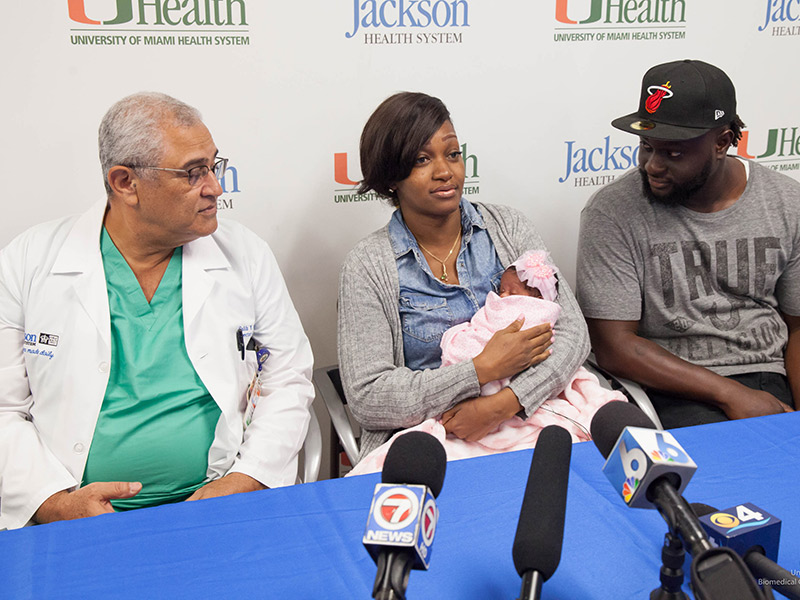 Joy Miller holding her daughter as she speaks at a press conference with her doctor and husband at her side