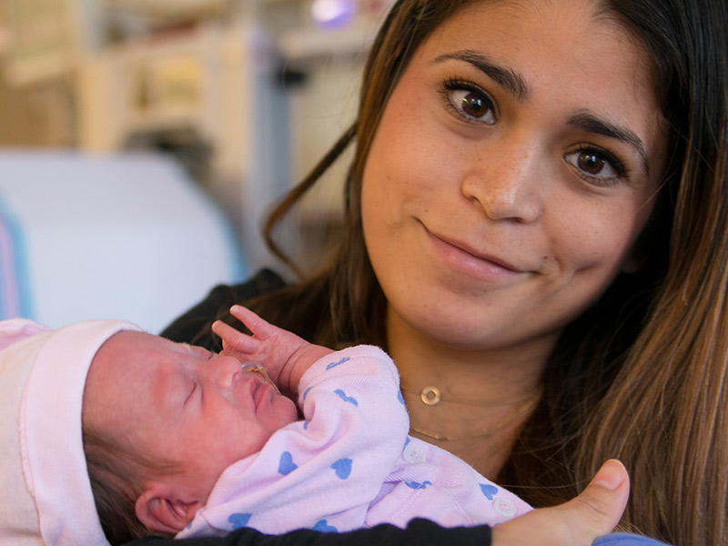 Michelle Castañeda smiling at the camera and holding her daughter