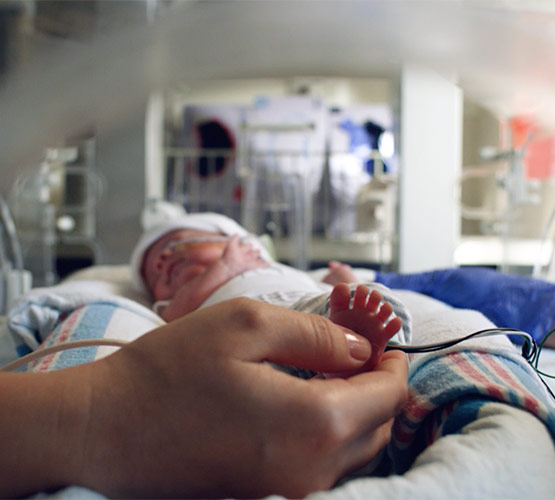 A newborn baby sleeping in an intensive care unit as the mothers hand touches the baby's foot