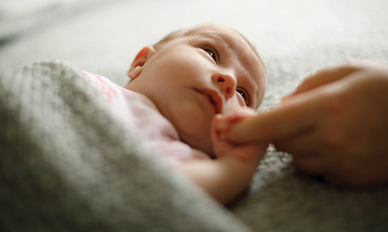 Baby girl laying down and holding its parents index finger as she looks towards her parent