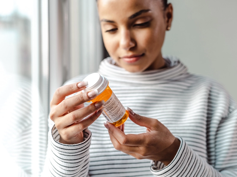Close-up of a woman examining an orange medication bottle.