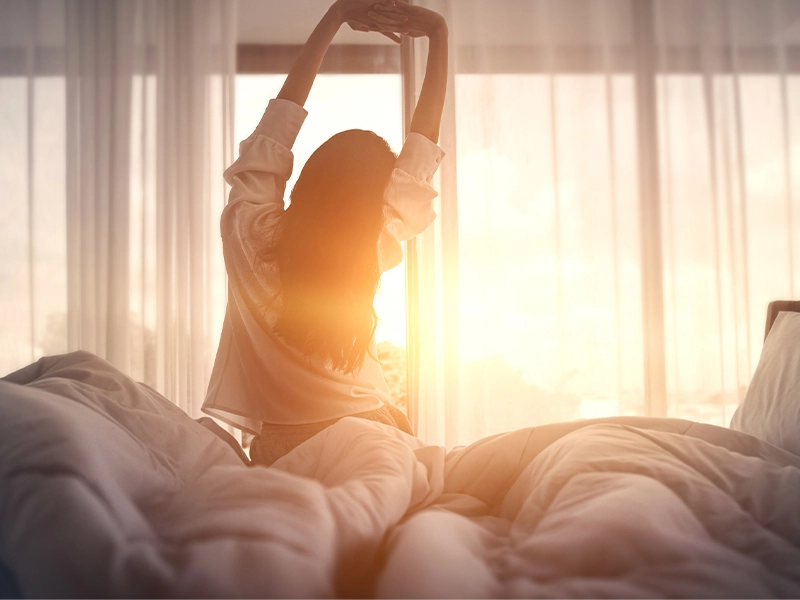 woman sitting on her back on the edge of her bed while stretching