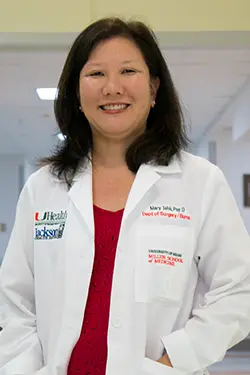Headshot of a medical professional, she smiles at the camera, she has dark short hair, and has on a white coat